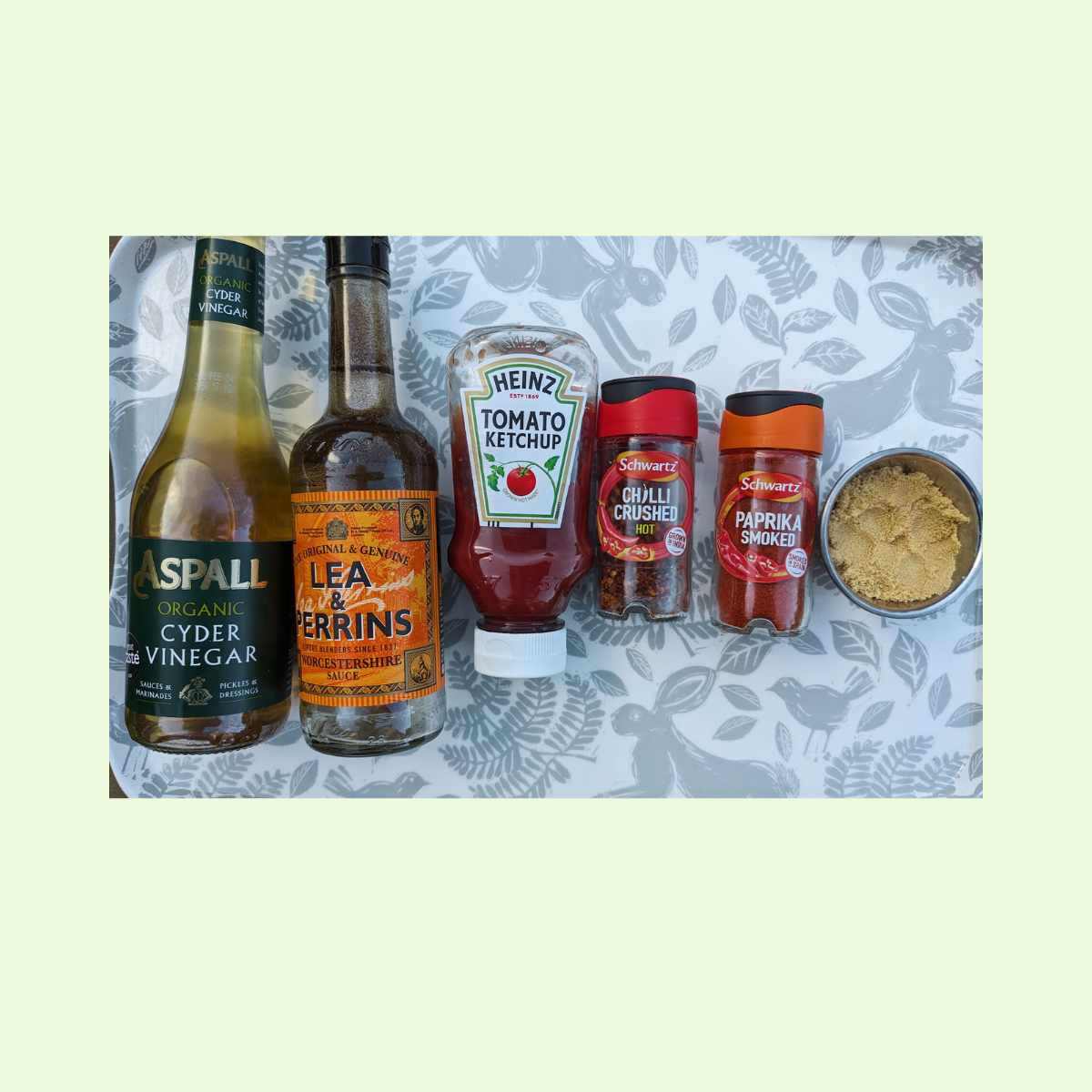 Bottles of Cyder vinegar, Worcestershire Sauce, Tomato Ketchup alongside jars of chili flakes, smoked paprika and a pot of brown sugar.