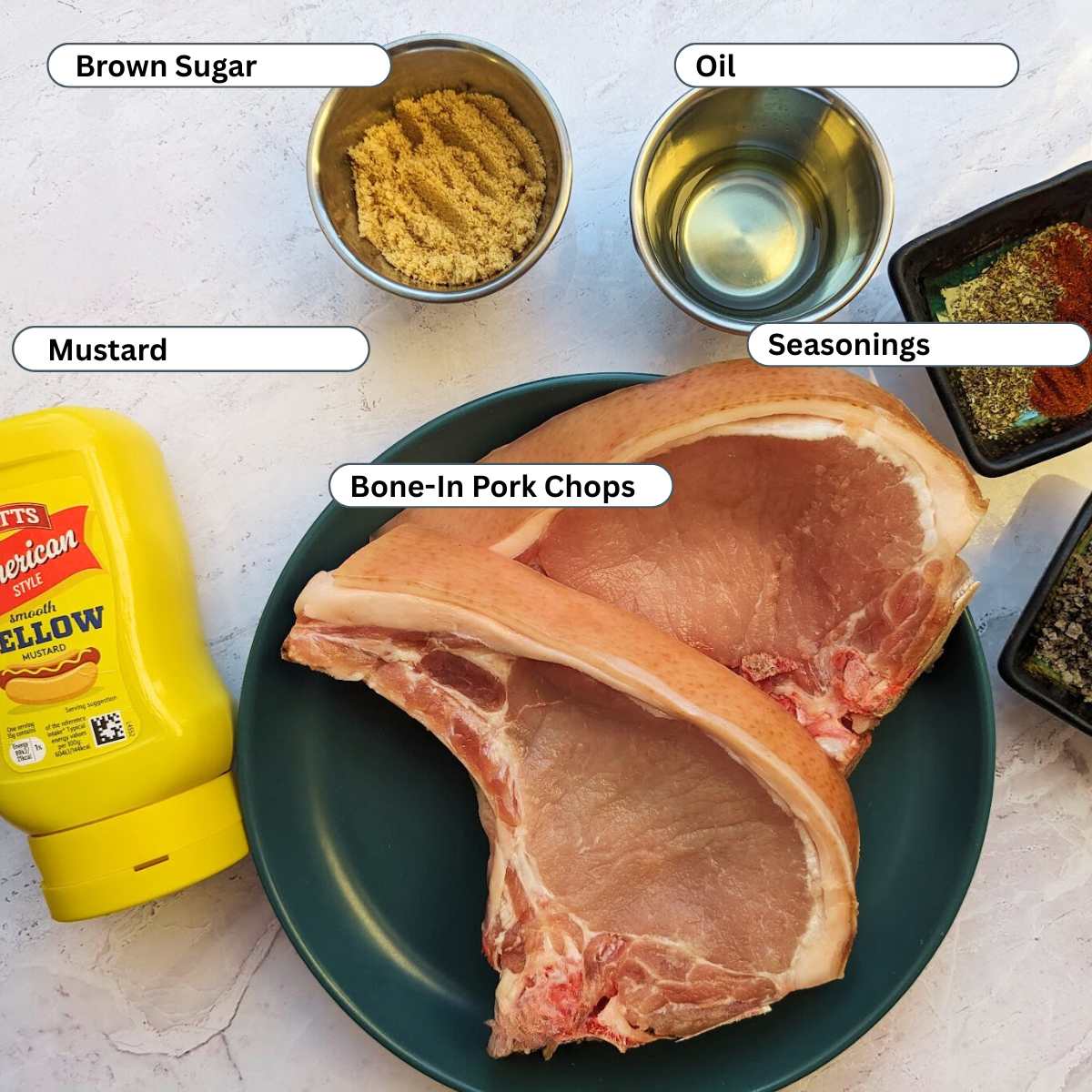 Ingredients for bone-in pork chops including pork chops, mustard, brown sugar, oil and seasonings on a kitchen board.
