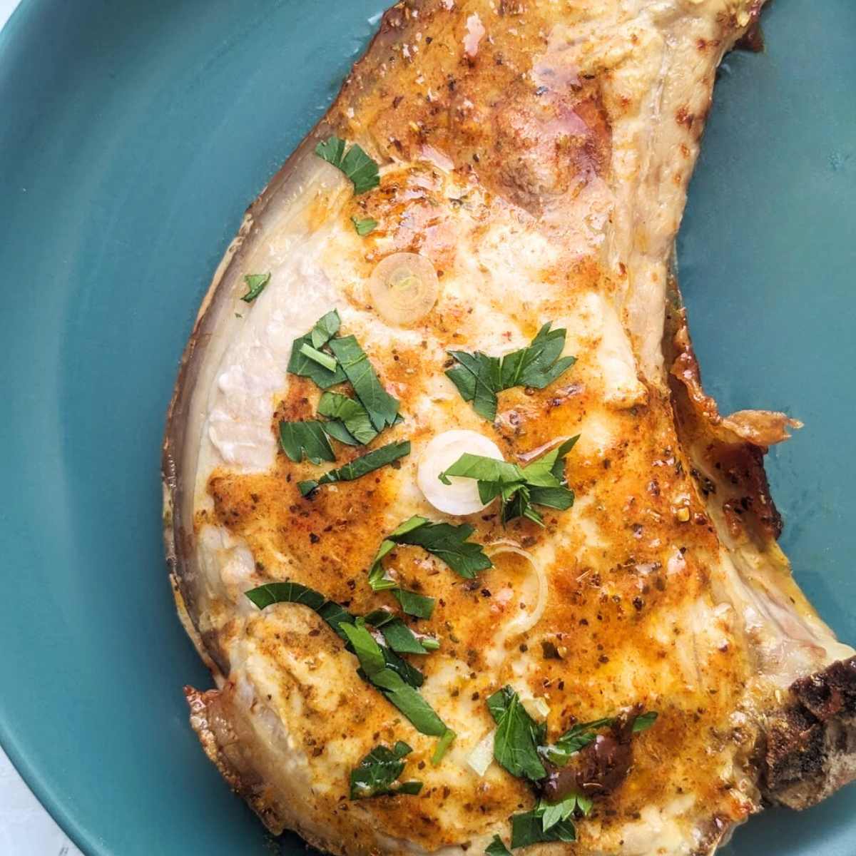A pork chop with a glaze sits on top of  a blue plate.