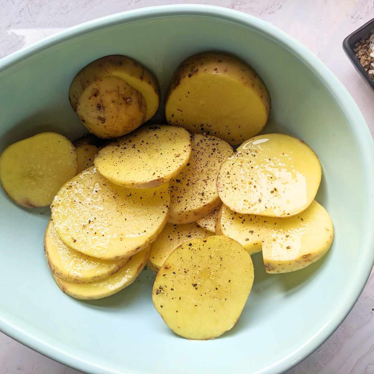 Sliced potatoes coated in oil and seasoning, in a blue mixing bowl.