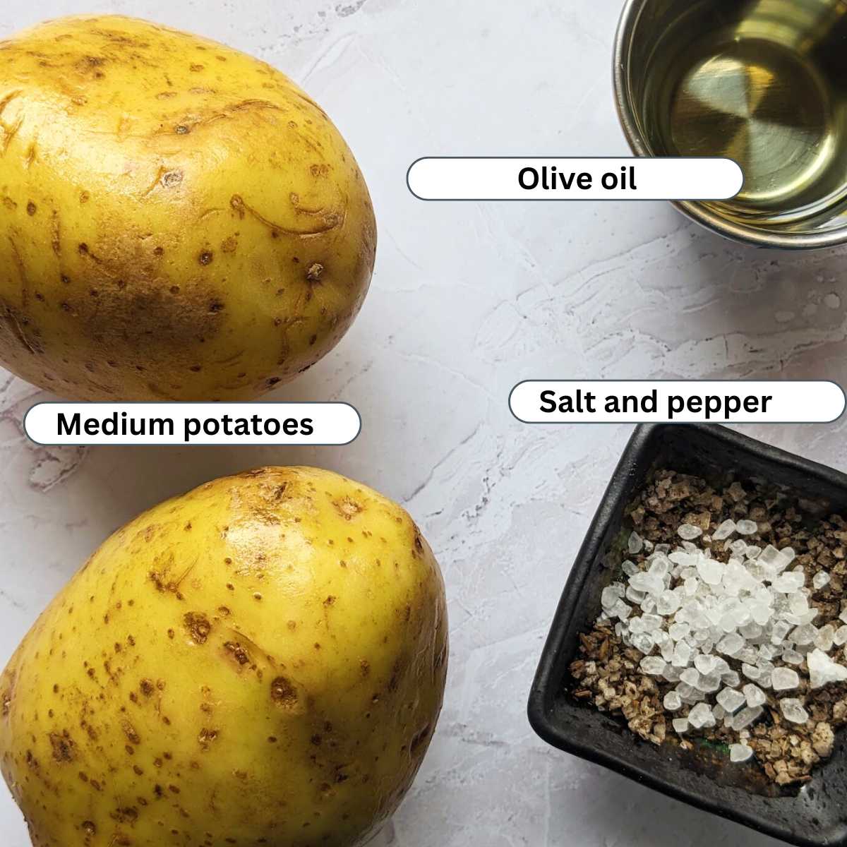 Two potatoes alongside a small pot of olive oil and a small dish containing salt and pepper.