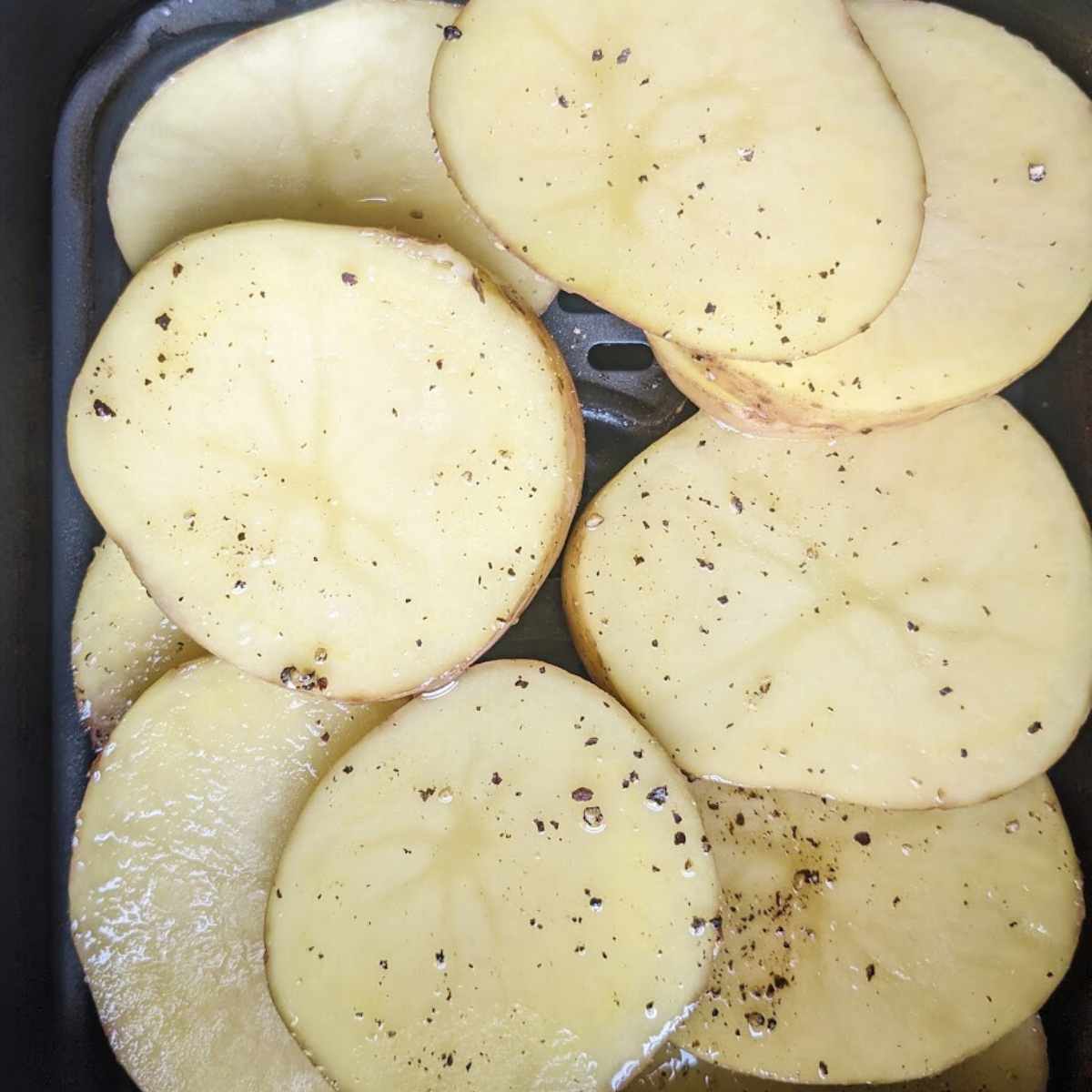 Potato slices in an air fryer basket.