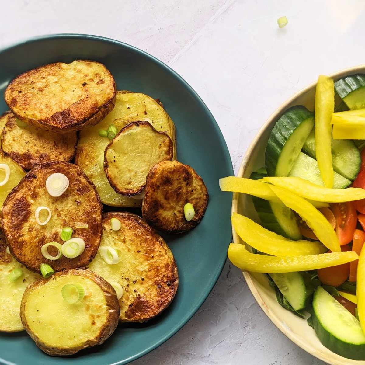 Air fried sliced potatoes on a blue plate with a bowl of salad vegetables in another bowl alongside.