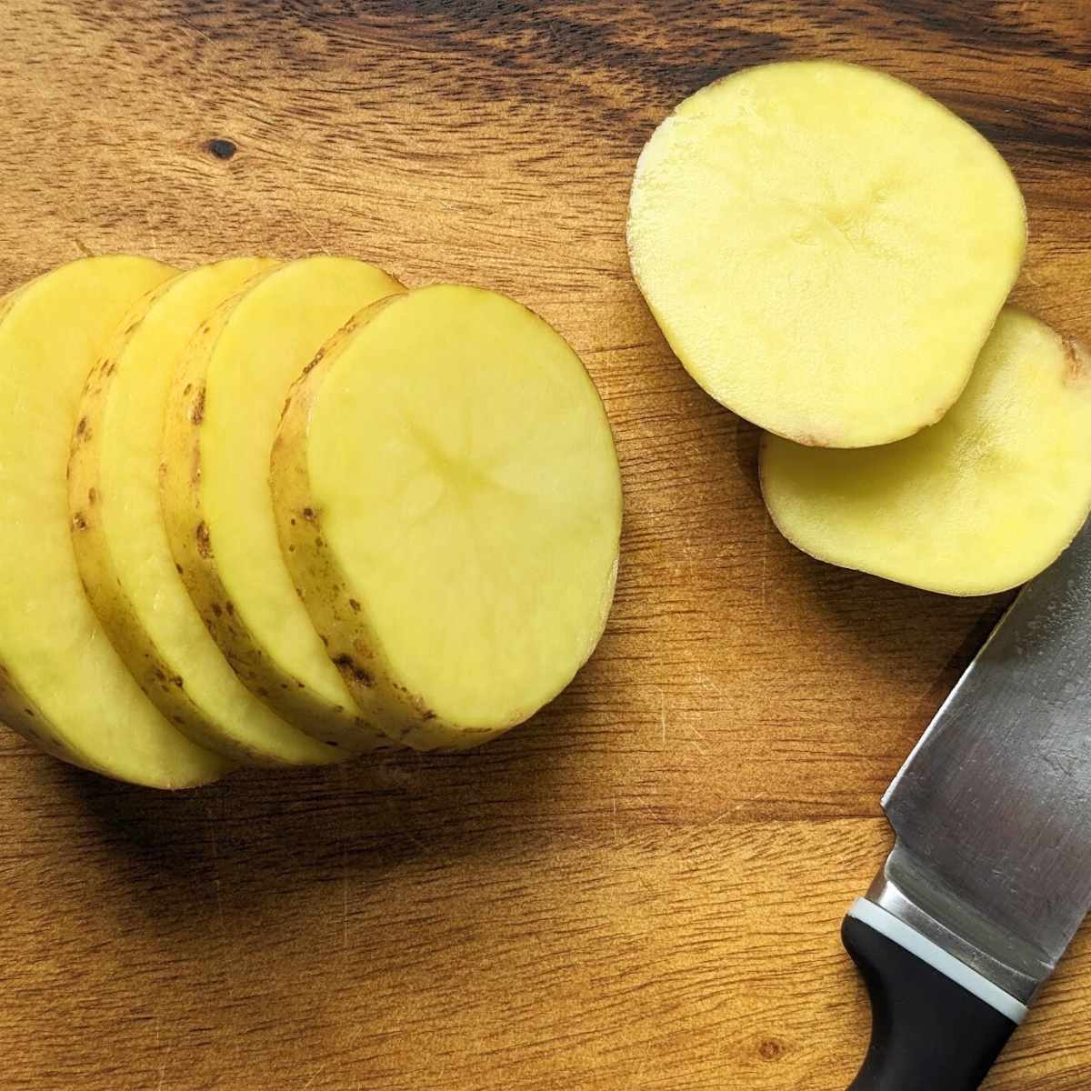 A raw potato cut into slices on a chopping board.
