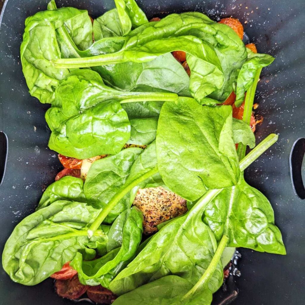 Spinach leaves on top of cooked cheese and roasted tomatoes