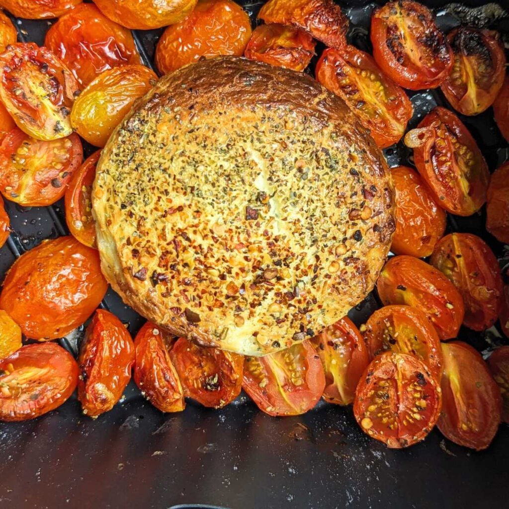 A cooked round of soft cheese in air fryer basket, surrounded by tomatoes.