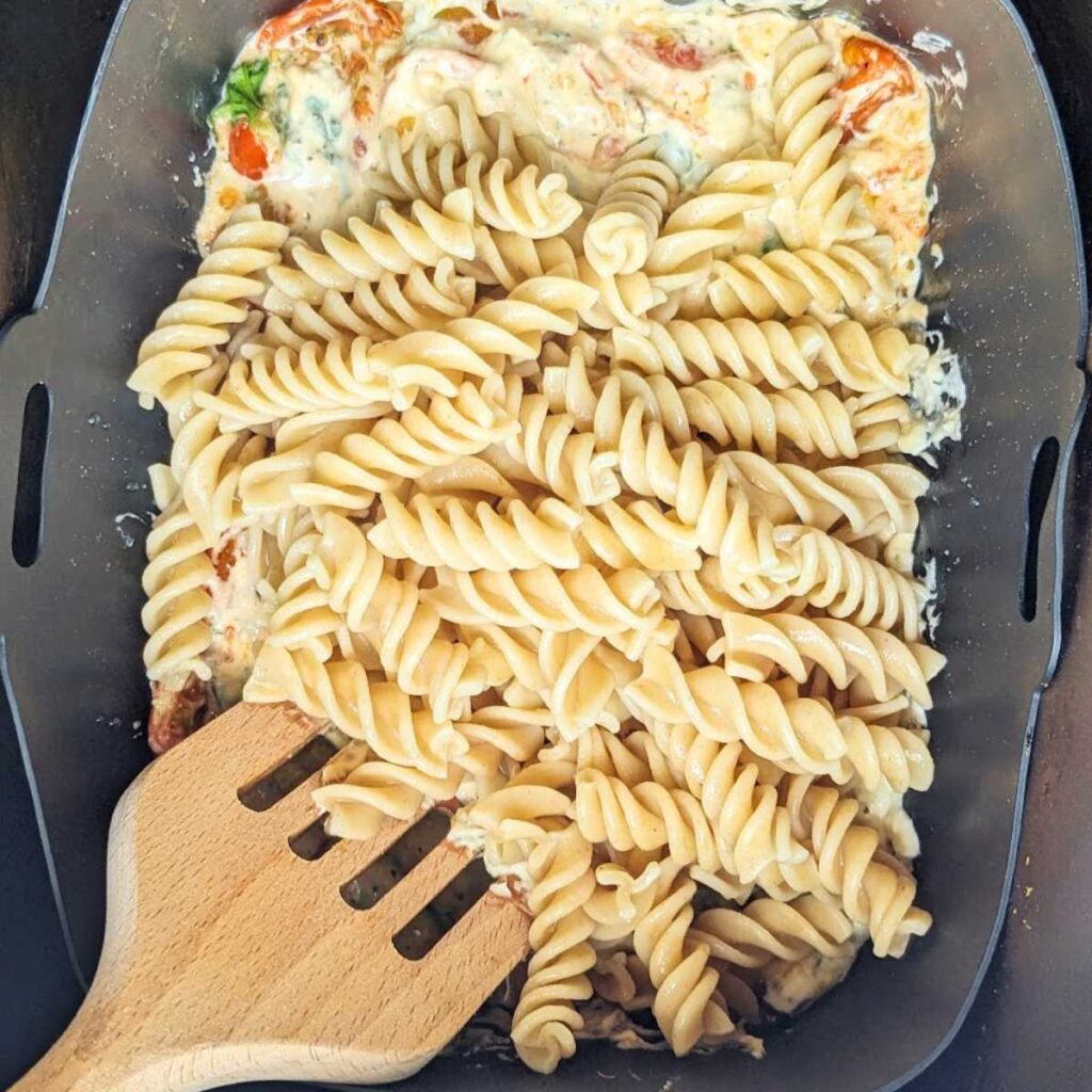 Cooked pasta is being stirred into pasta sauce in air fryer silicone liner.