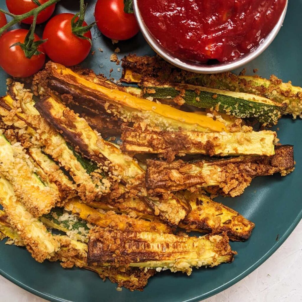 A plate of zucchini fries with a tomato dip on the side and fresh tomatoes.