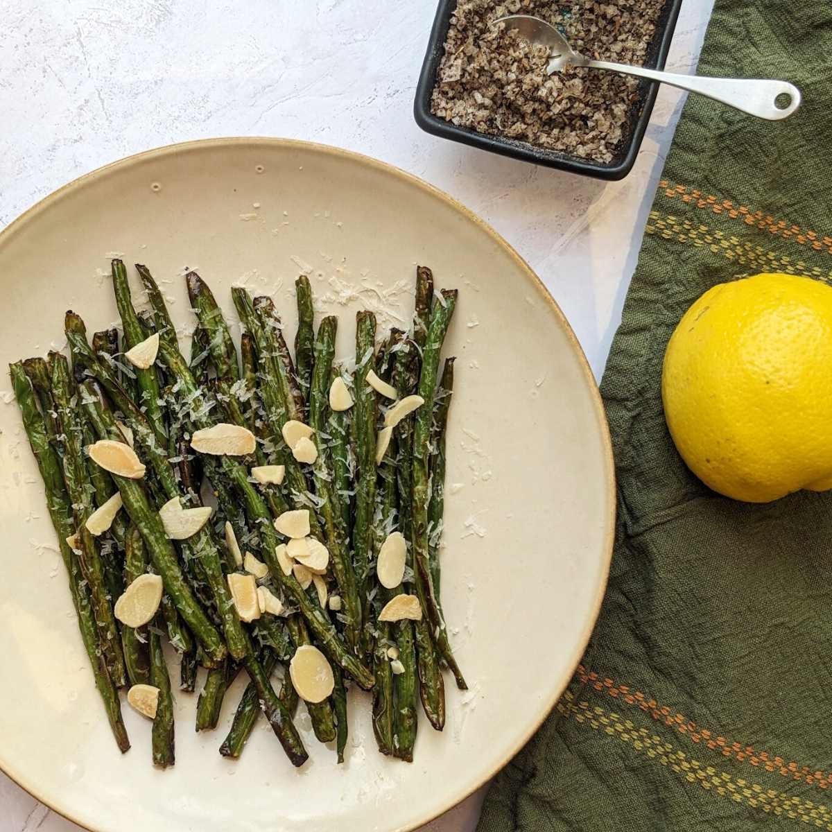 Air fryer green beans on a plate with seasoning and a lemon alongside.