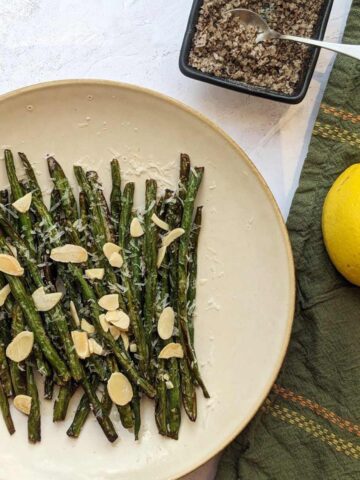 Fried green beans on a plate with a napkin, seasoning and a lemon at the side.