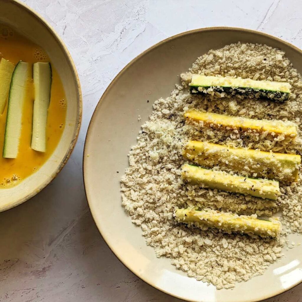 Zucchini being dipped into an egg mixture and panko breadcrumbs.