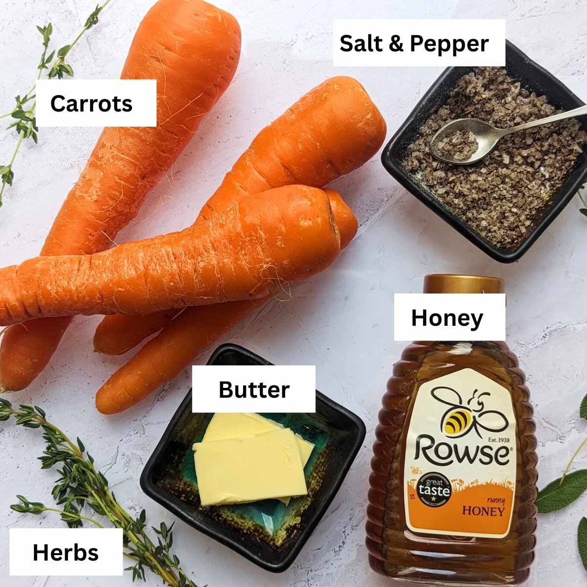 A board with the ingredients for air fryer honey carrots on it, including carrots, butter, honey, salt and pepper and fresh herbs.