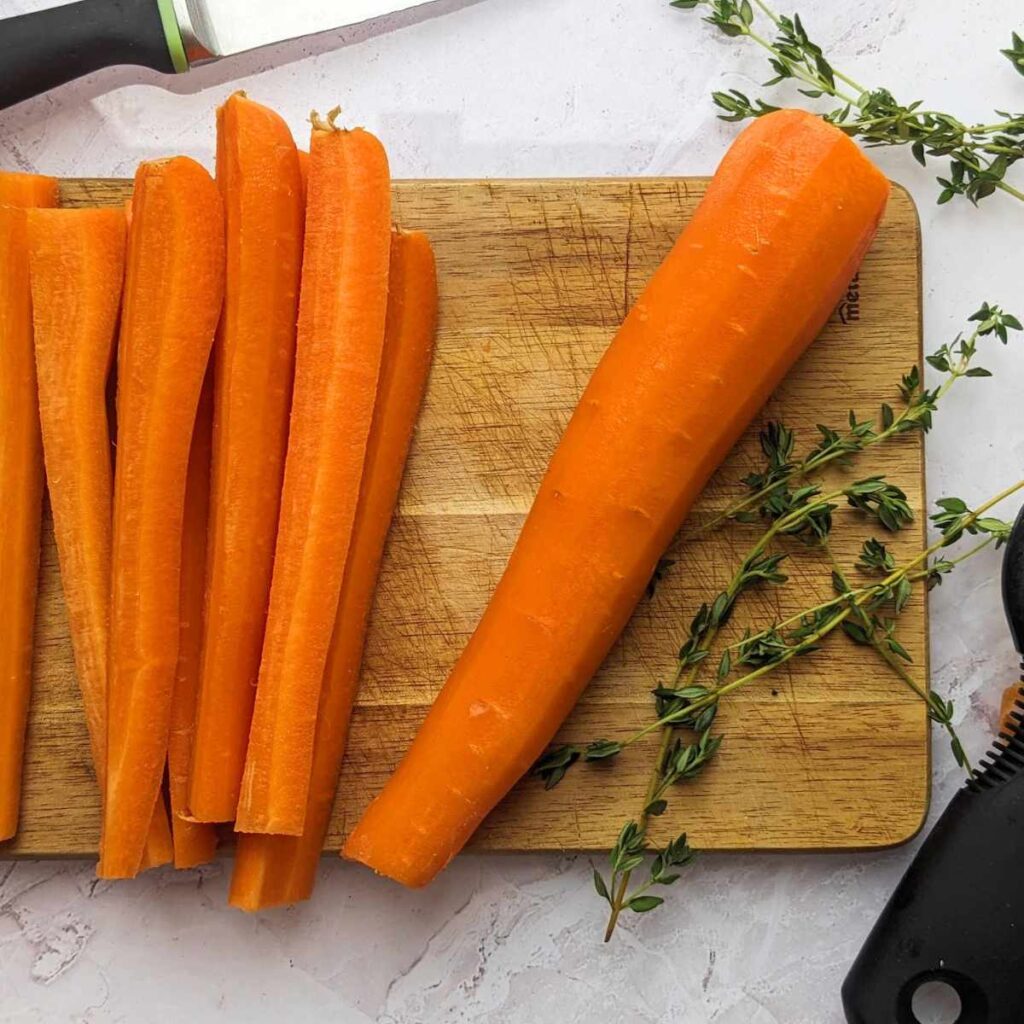 Raw carrots on a chopping board with a peeler at the side.