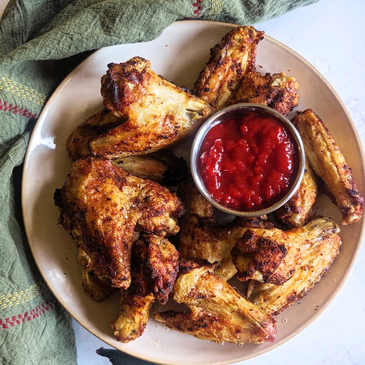 Air fryer chicken wings on a plate with a tomato dip.