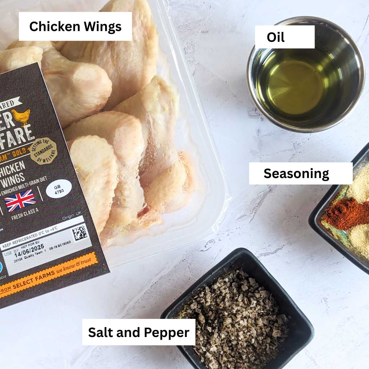 Ingredients for air fryer fried chicken laid on a kitchen worktop. Includes a box of chicken wings, oil, seasoning, salt and pepper.