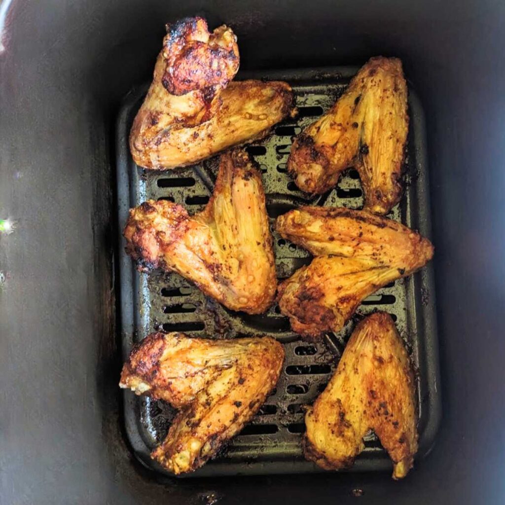 Cooked chicken wings in air fryer basket.