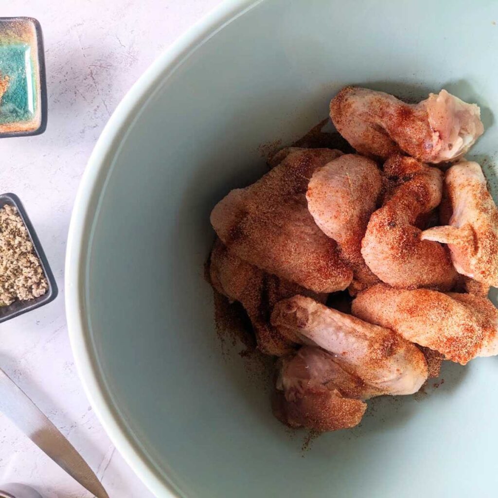 Raw chicken wings in a bowl, coated in season.