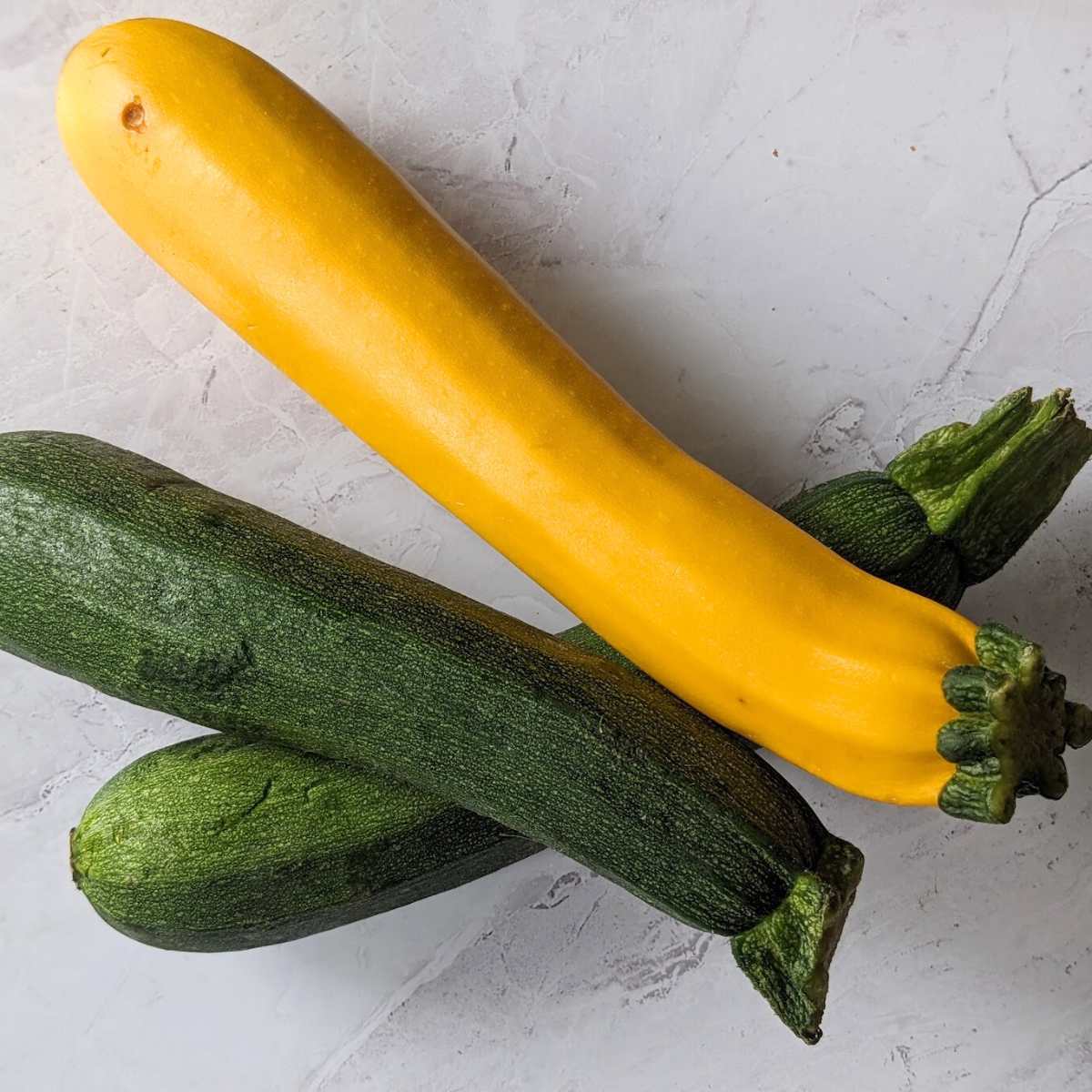 Two green zucchini and one yellow zucchini on a board.