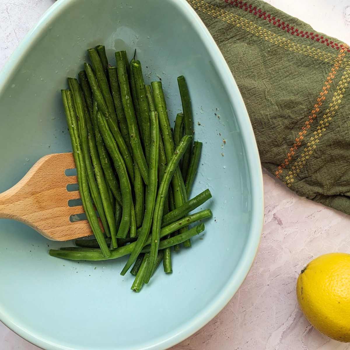 Green beans being mixed with oil and seasoning in a large blue bowl.
