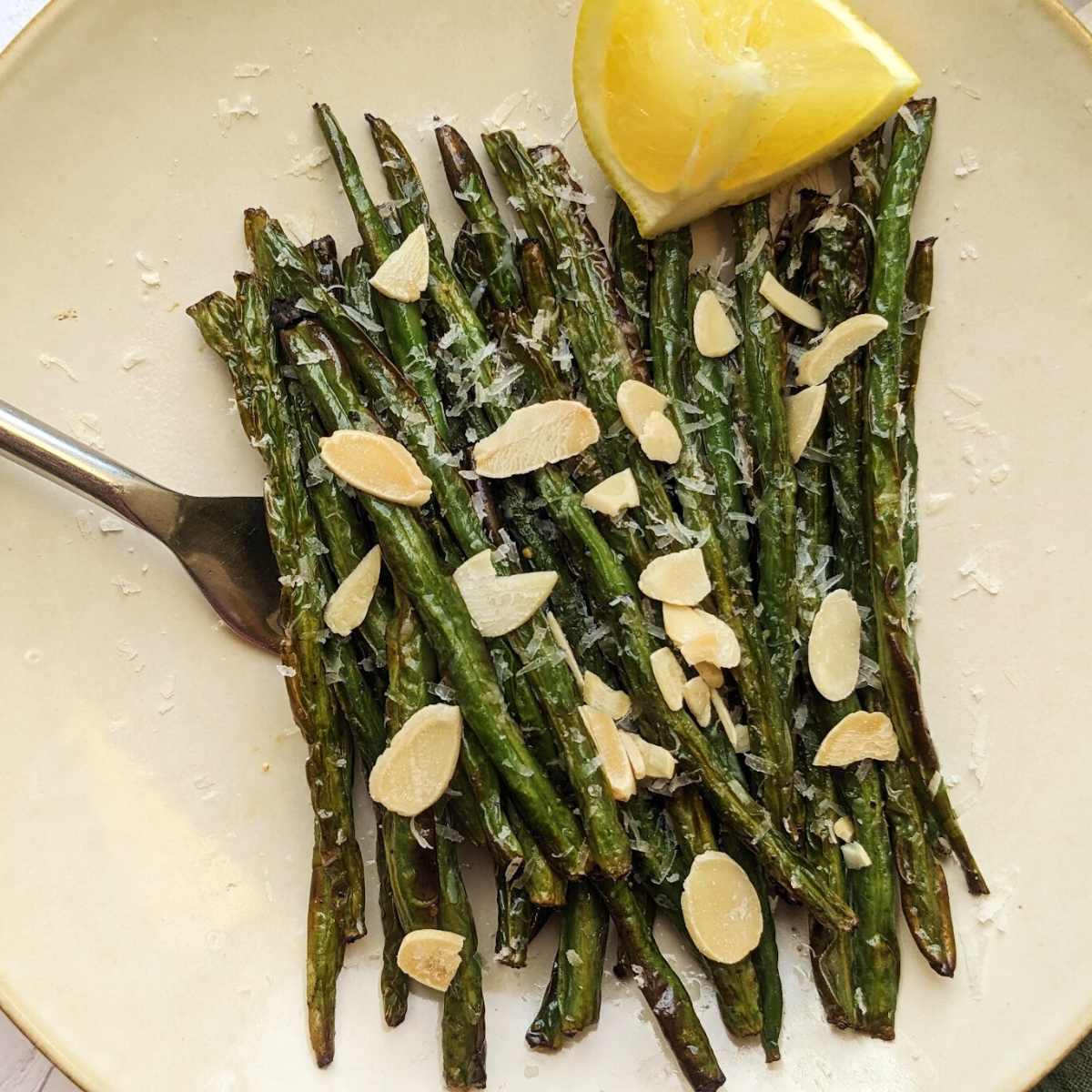 Air fryer green beans on a serving plate with a wedge of fresh lemon.