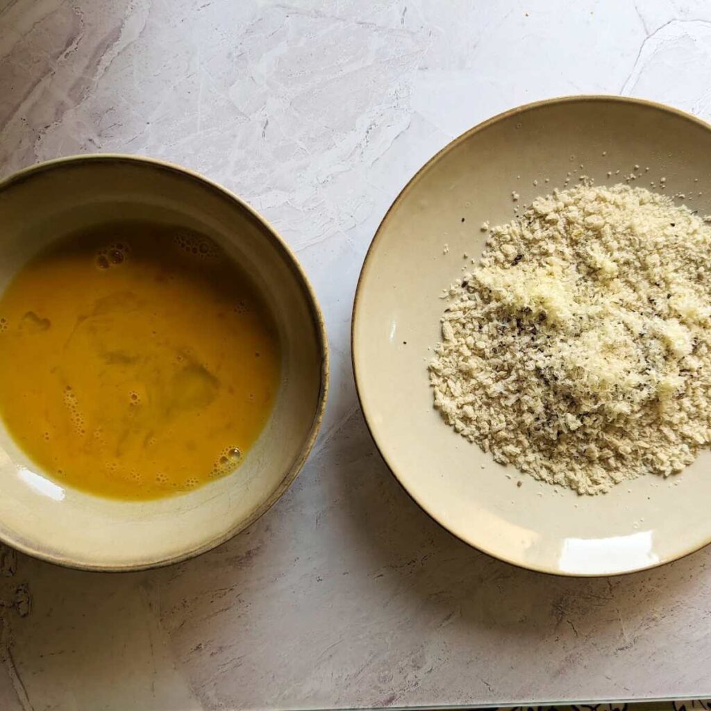 A bowl containing panko breadcrumbs and another bowl with a whisked egg.
