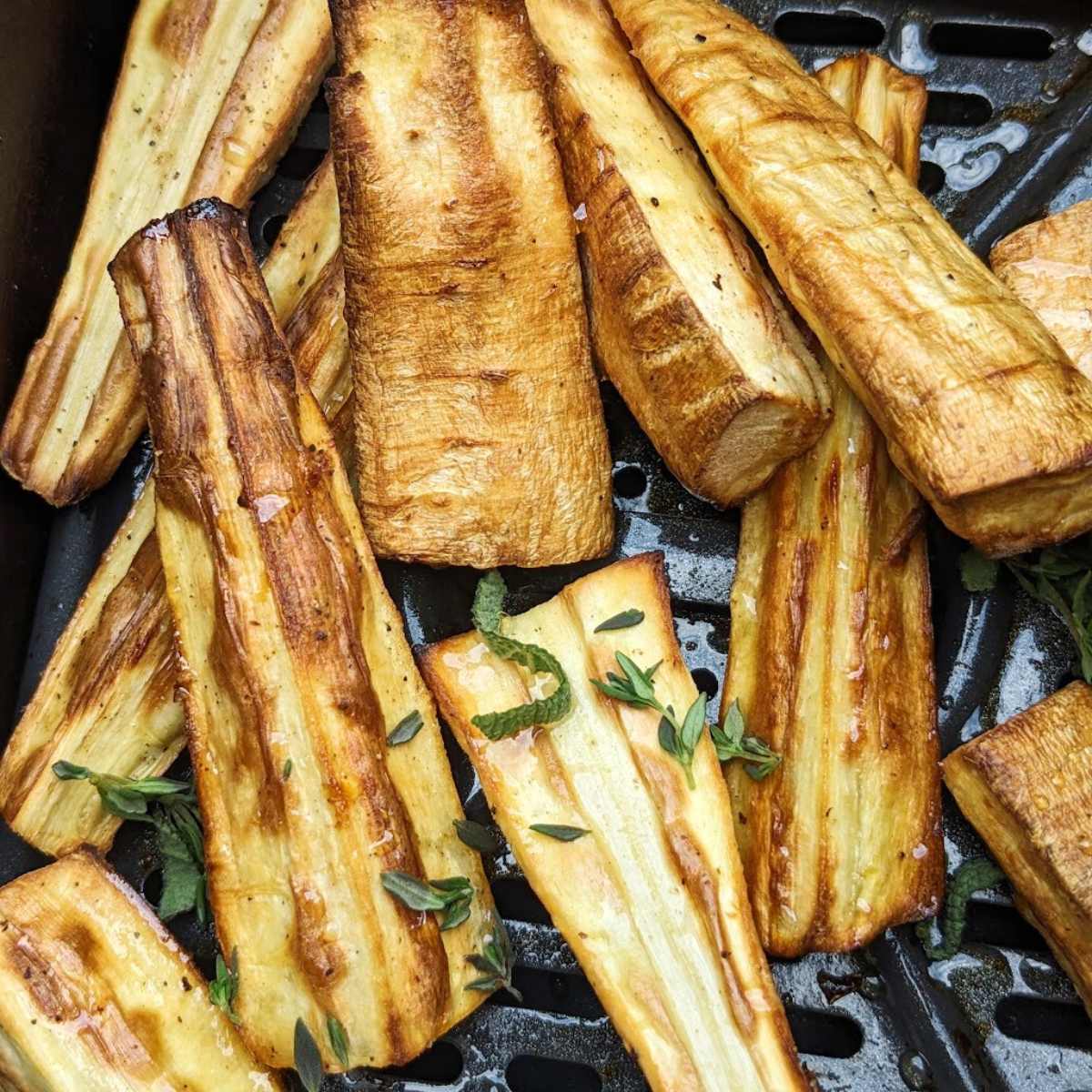 Parsnips roasting in an air fryer basket.