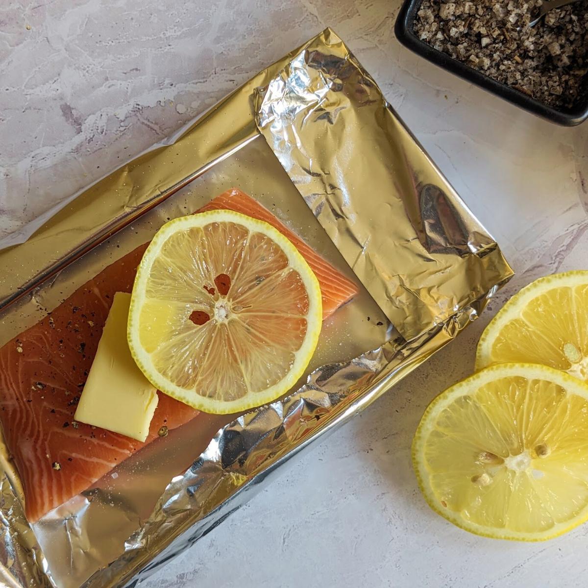 Salmon fillet with slices of lemon and butter on top on a piece of kitchen foil.