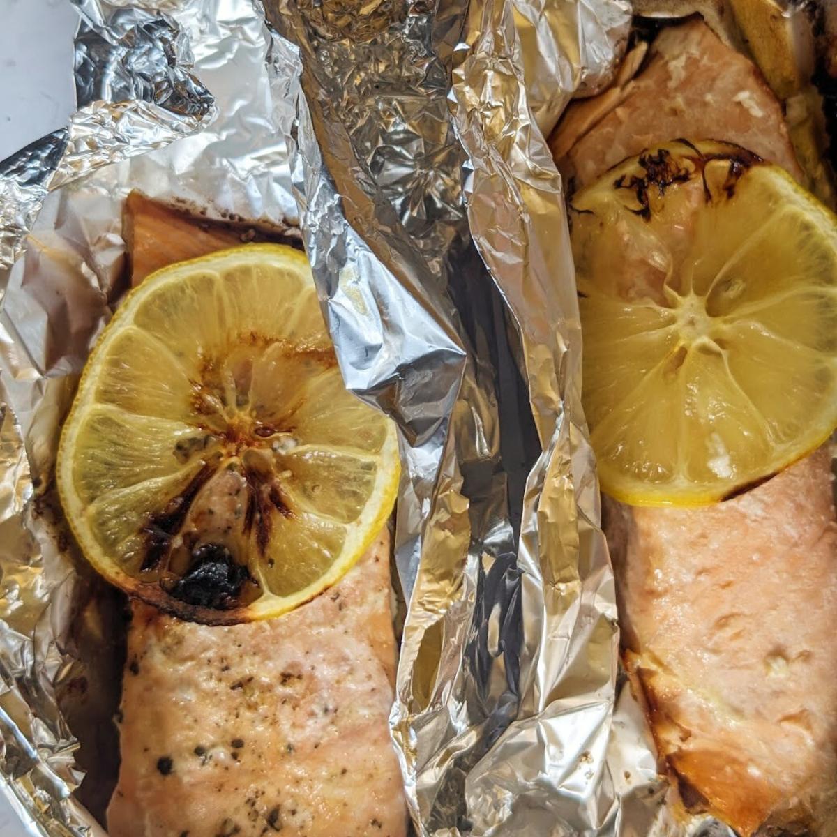 Two foil parcels have been opened up to reveal the cooked salmon inside.