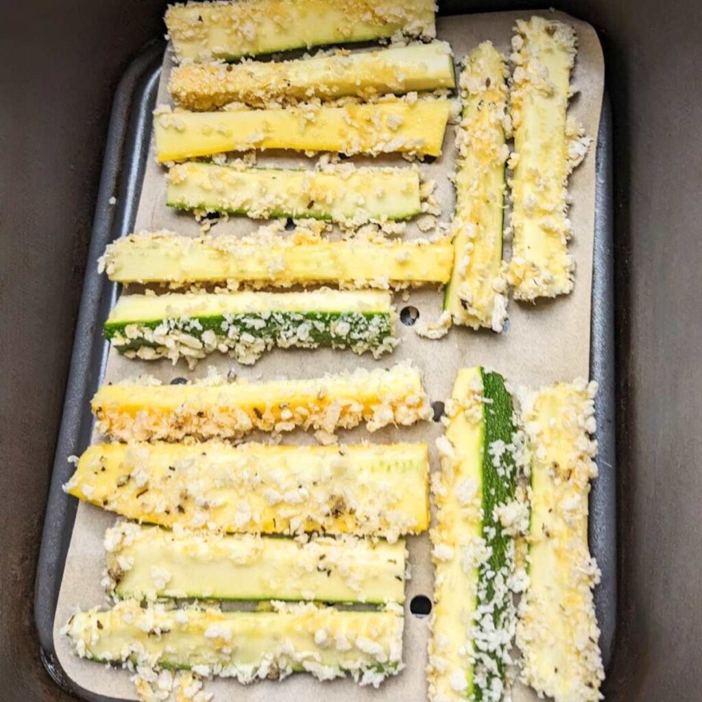 Air fryer basket with zucchini fries lined up inside.