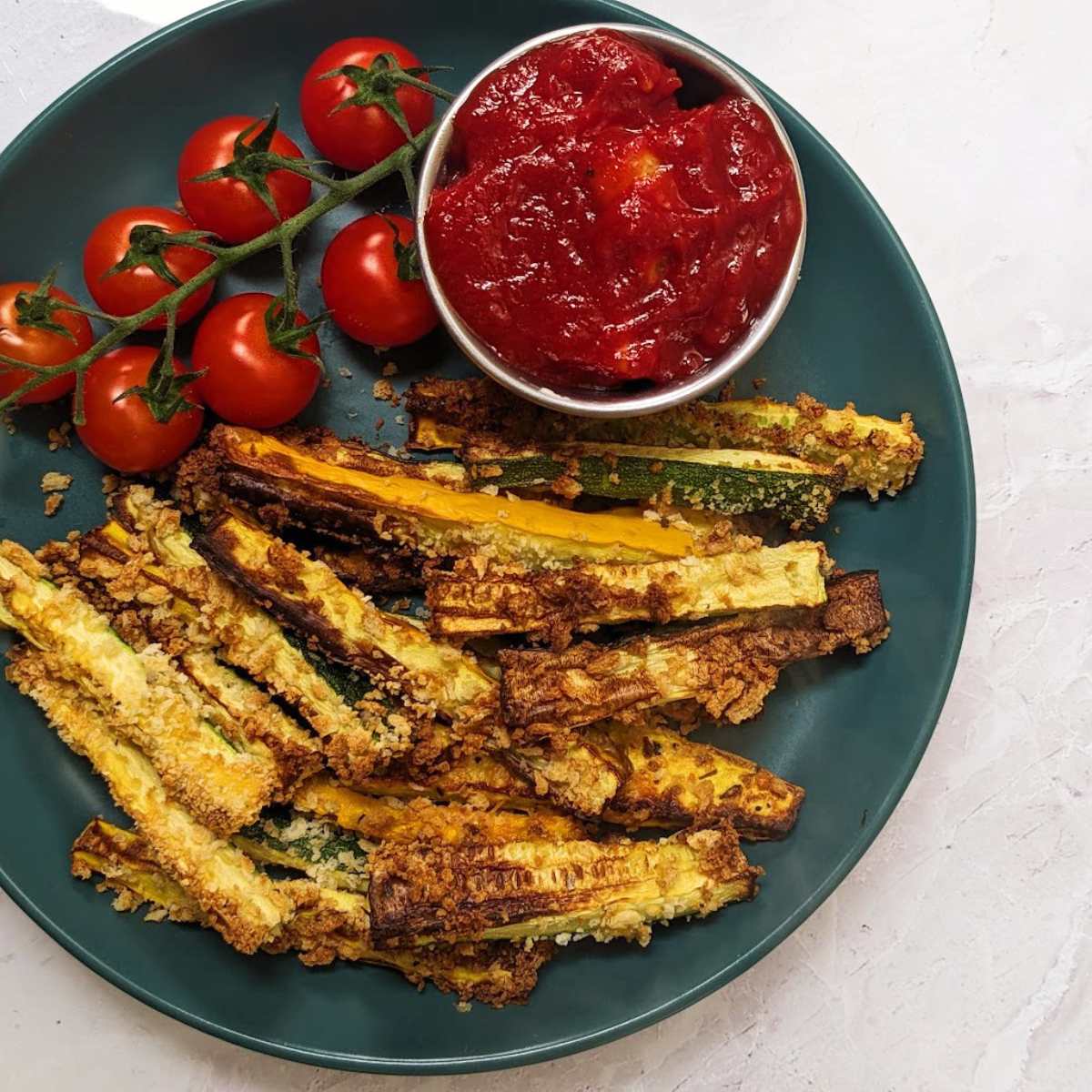 A plate of zucchini fries with fresh tomatoes and a tomato dip.