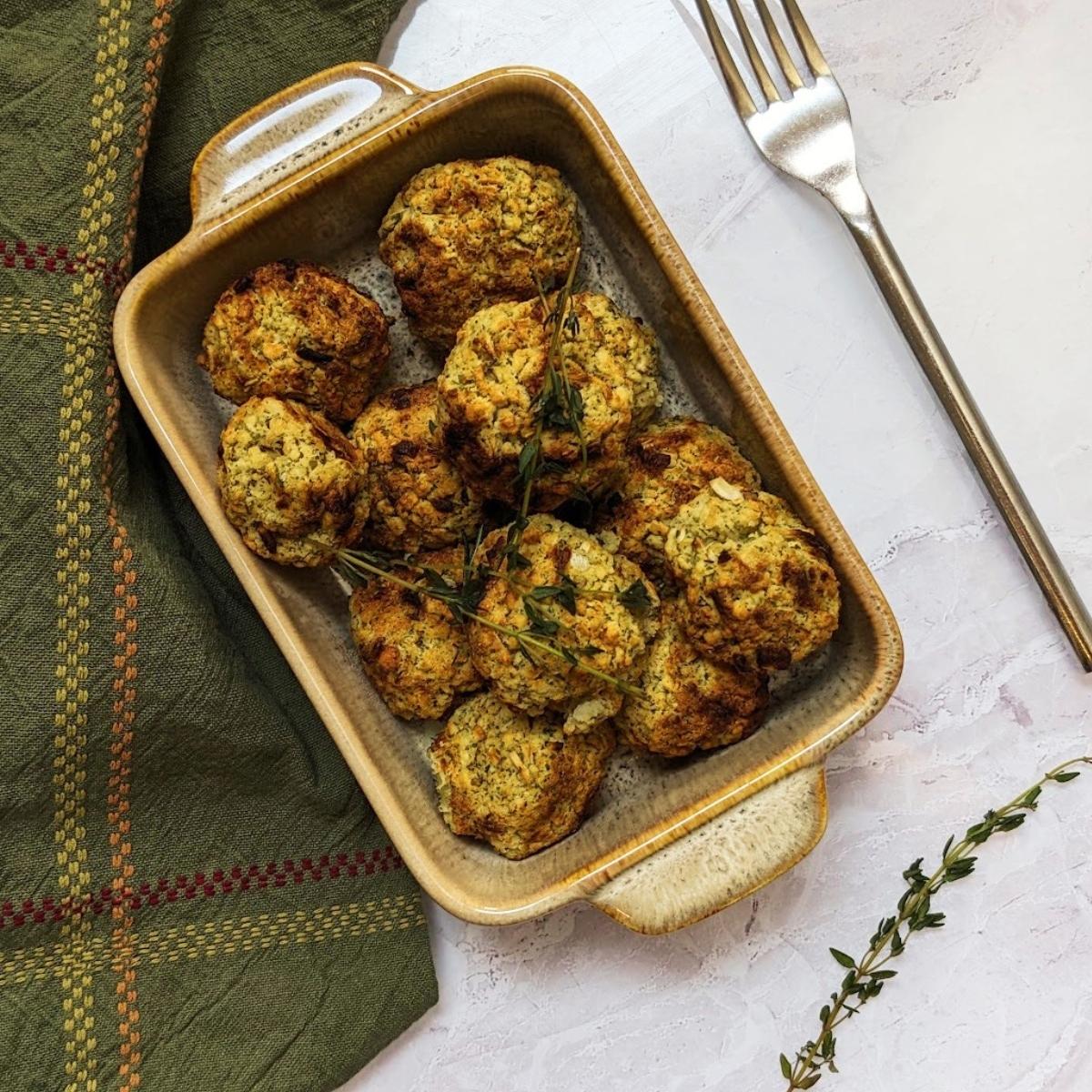 A serving dish filled with cooked stuffing balls on a kitchen work surface with a green towel and a fork at the side.