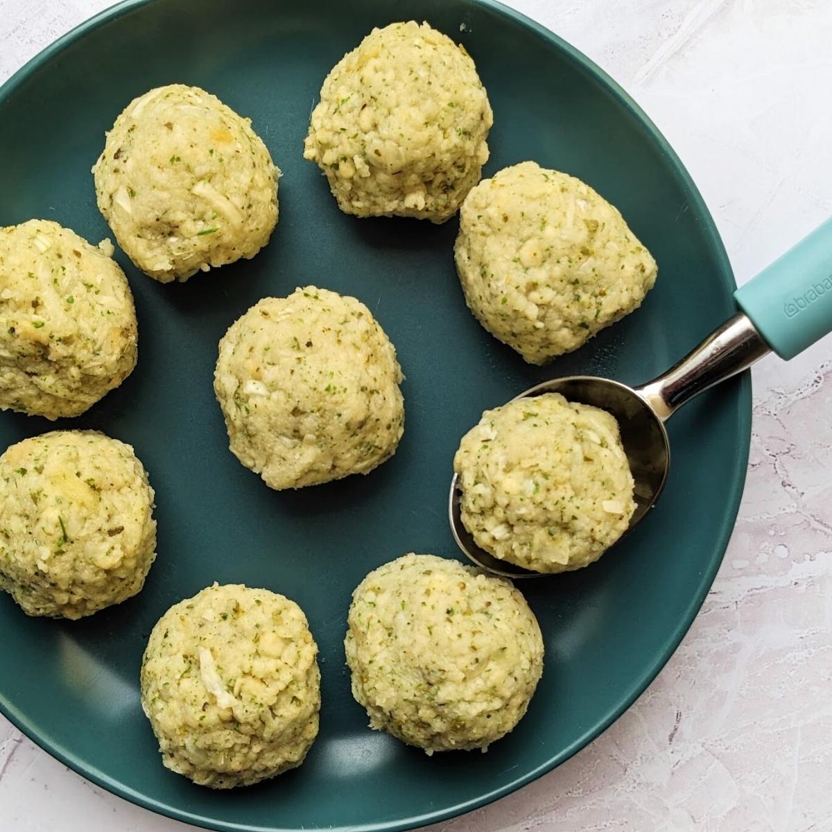 Nine stuffing balls on a round plate with an ice-cream scooper at the side.