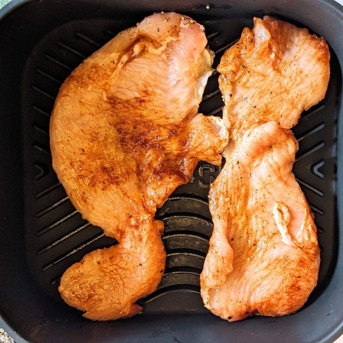 Two turkey steaks in an air fryer basket.