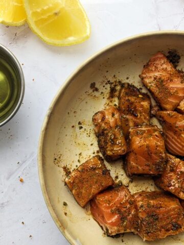 Salmon bites in a bowl with seasoning and lemon.