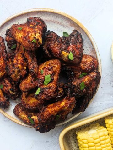 Air fried Buffalo chicken wings in a bowl with corn-on-the-cob and coleslaw in bowls by the side.