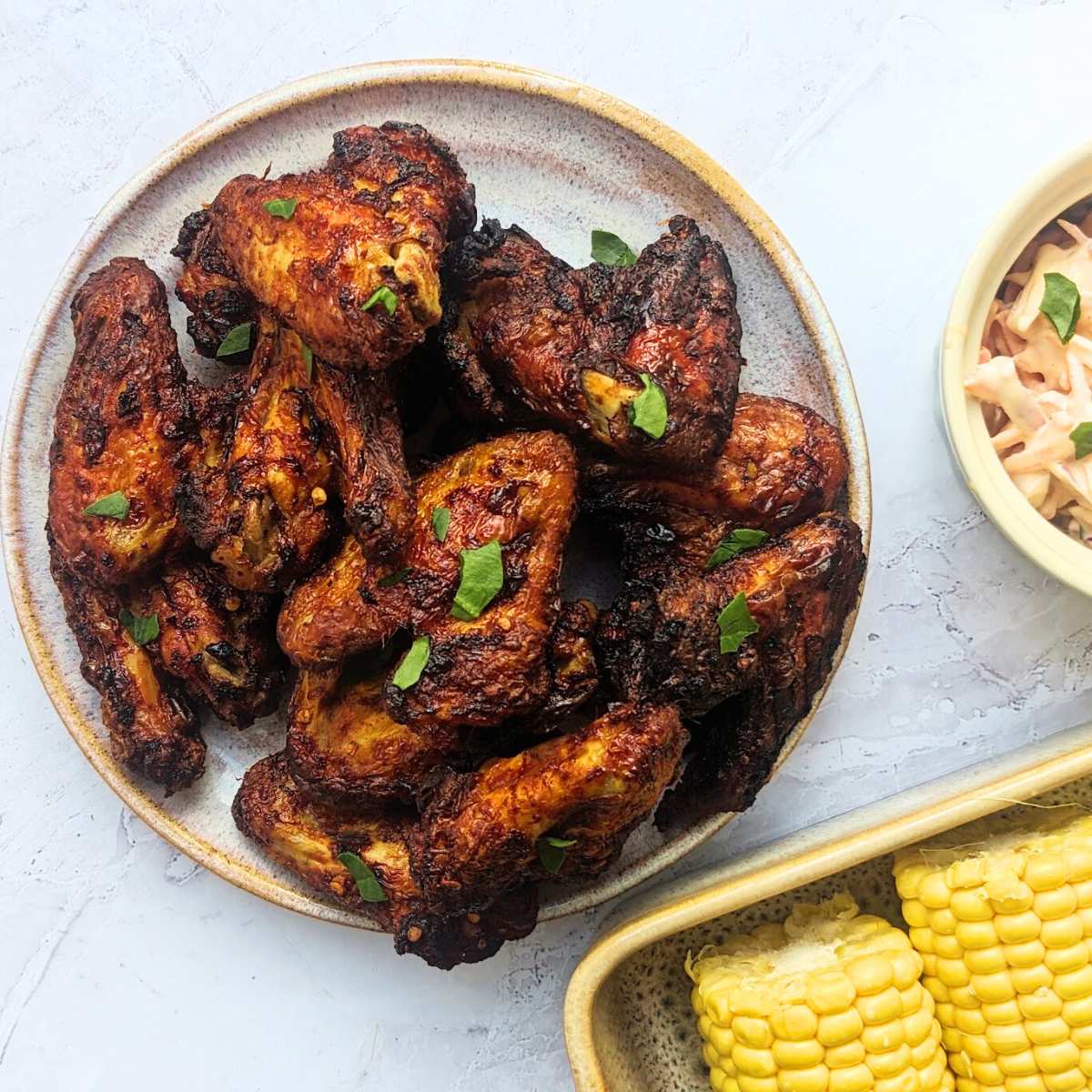 Air fried Buffalo chicken wings in a bowl with corn-on-the-cob and coleslaw in bowls by the side.