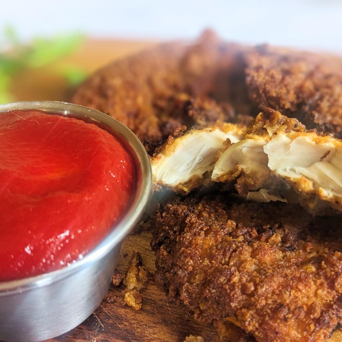 Chicken tenders on a board with a ketchup dip at the side.