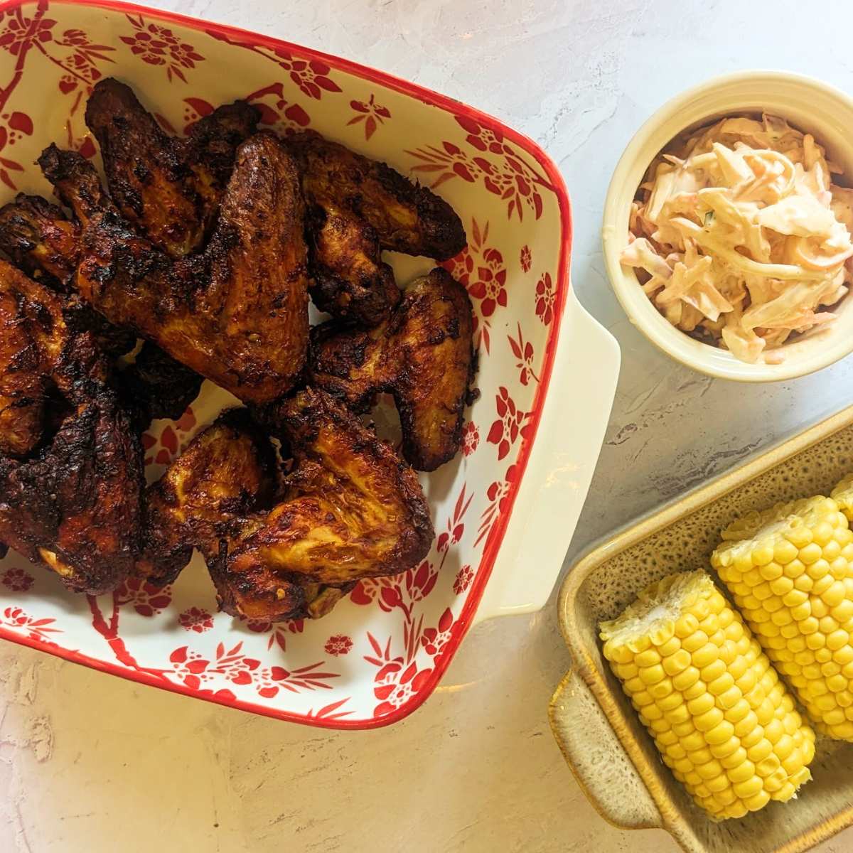 Air fried buffalo chicken wings in a bowl with side dishes of sweetcorn and coleslaw.
