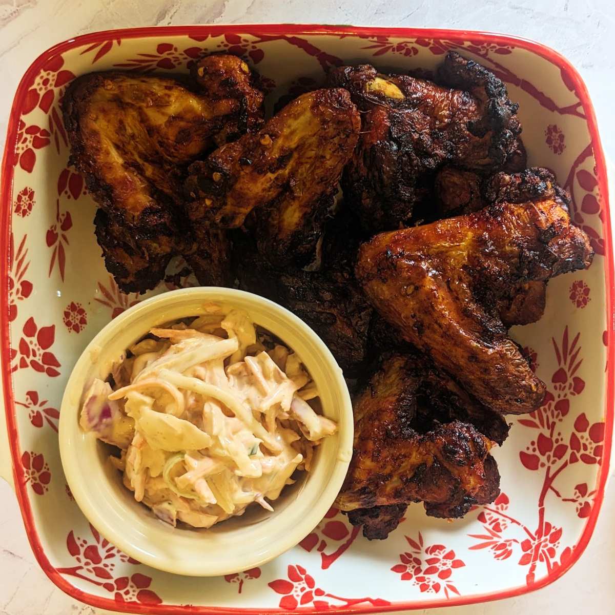 CHicken wings in a serving dish with a pot of coleslaw.