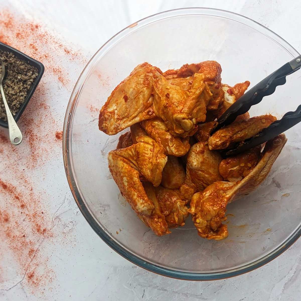 Chicken wings in a bowl being tossed with buffalo seasoning.
