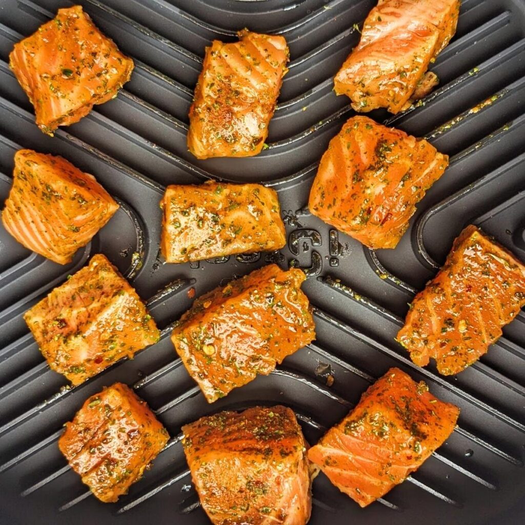 Seasoned, raw salmon pieces in an air fryer basket.