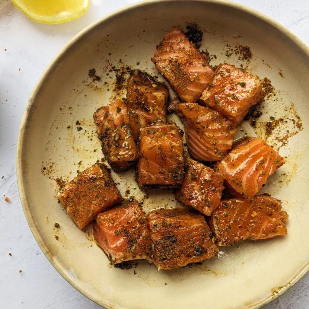 Raw cubes of salmon tossed in herbs and spices in a bowl.