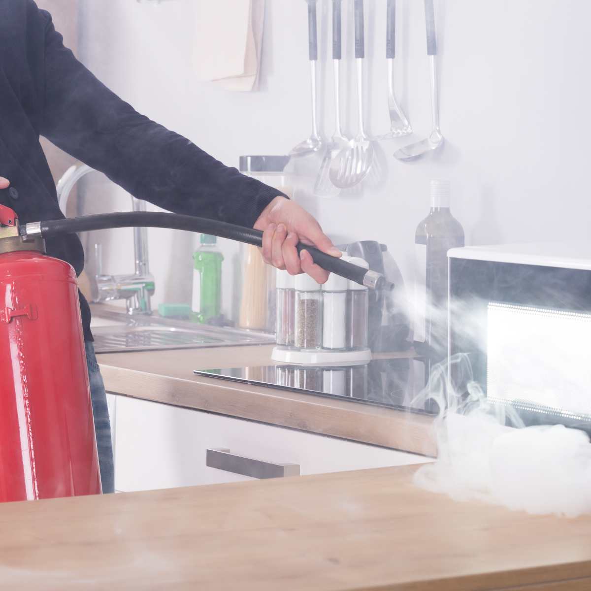 A person using a fire extinguisher directing it at a smoking appliance in the kitchen.