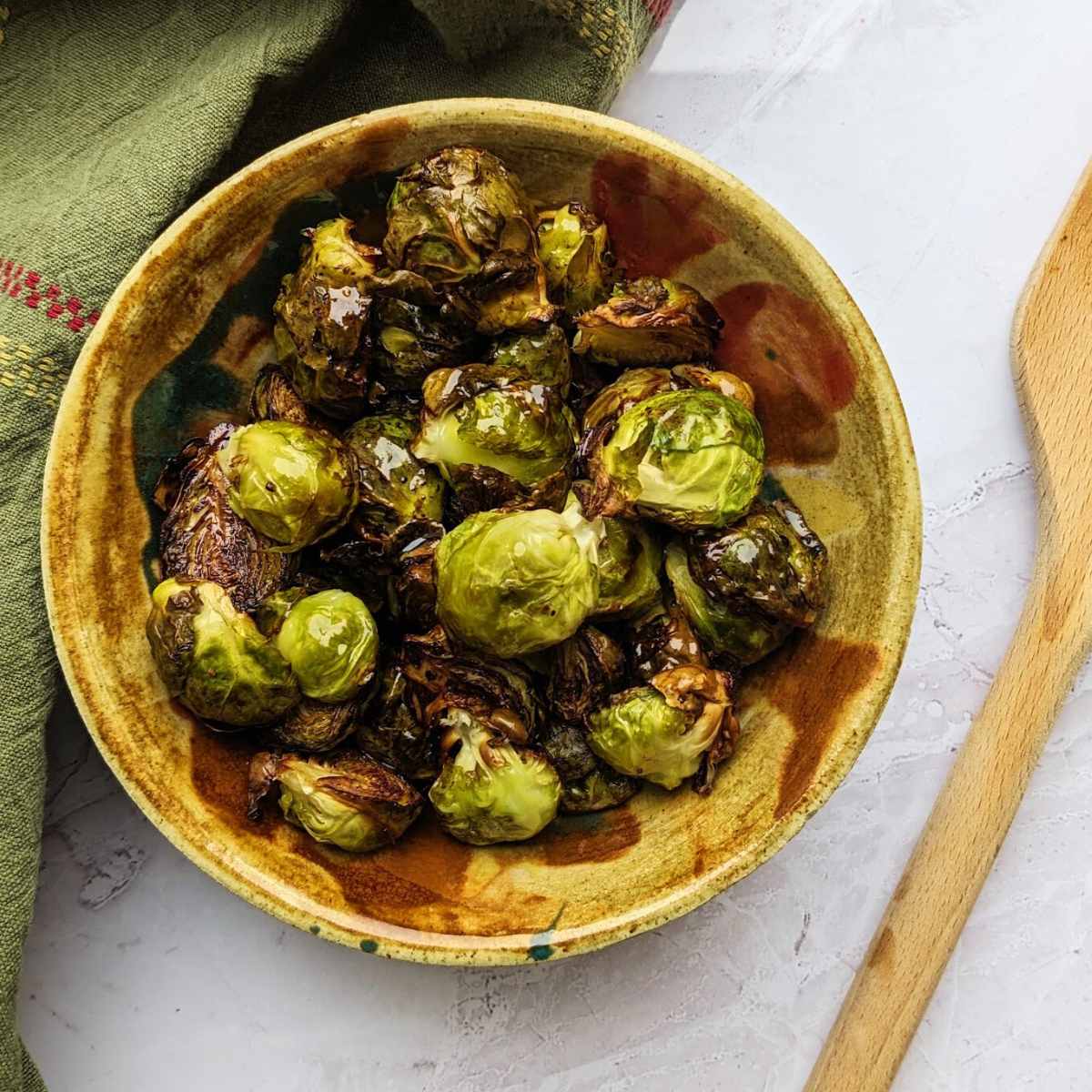 Balsamic Brussels sprouts in a bowl with a wooden spoon at the side.