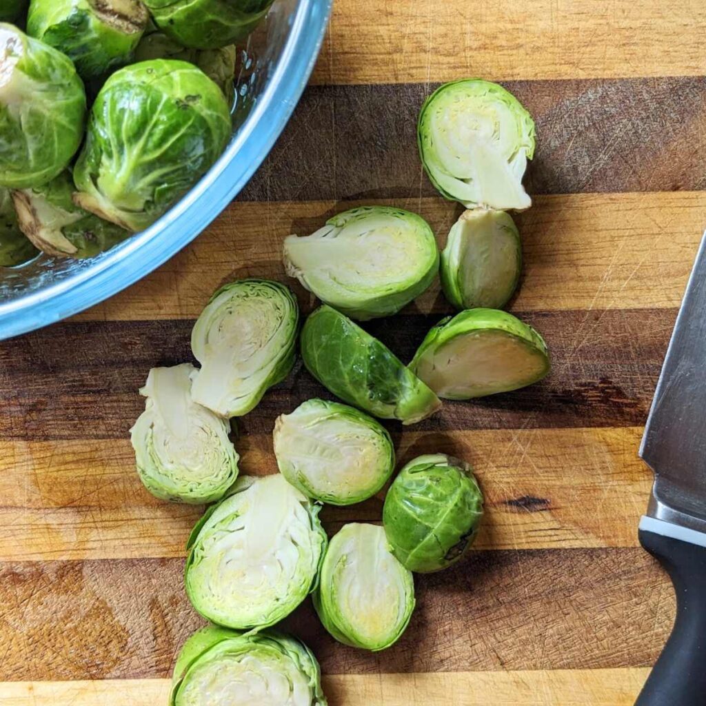 Brussels sprouts cut in half on a chopping board with a knife alongside.