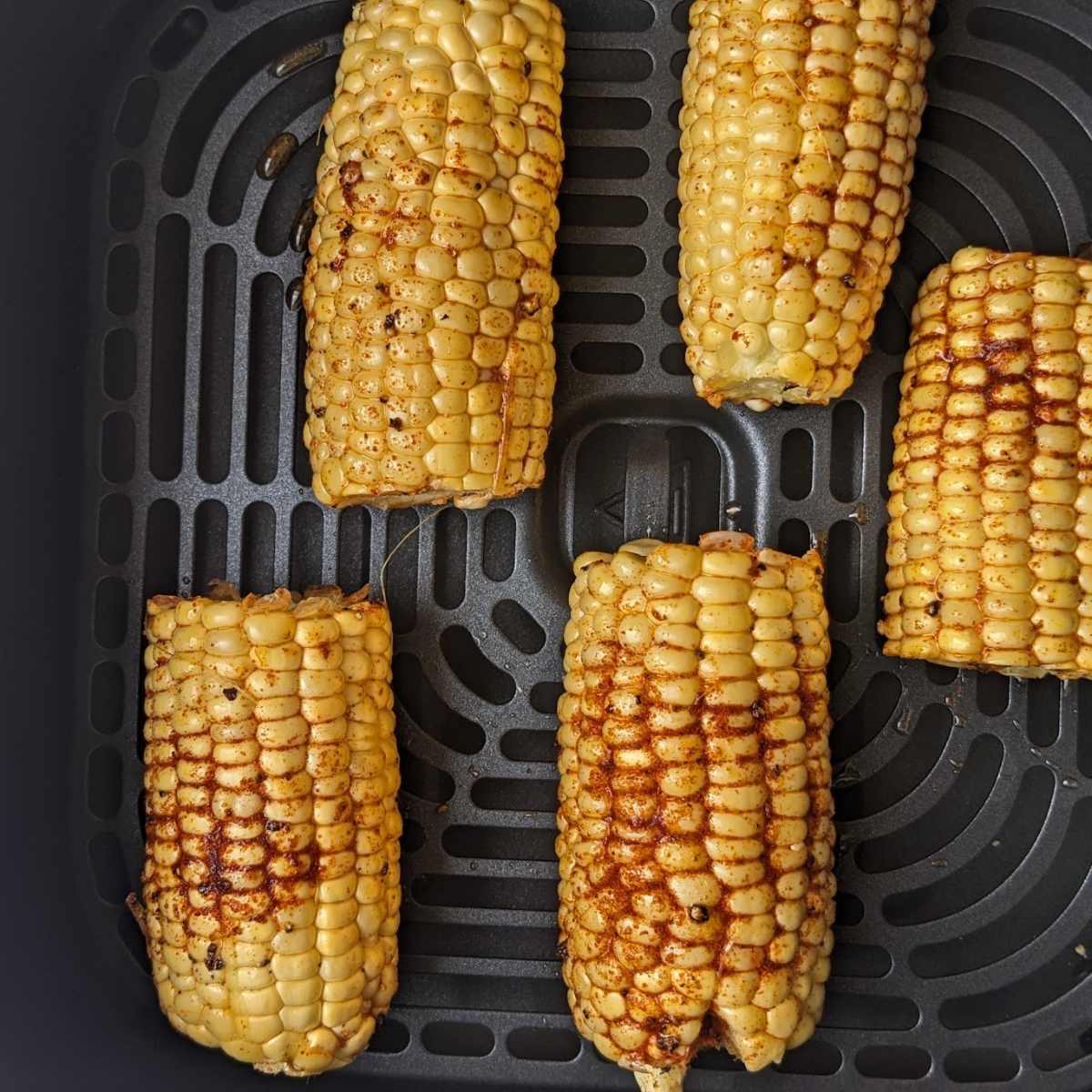 Corn on the cob in an air fryer basket.