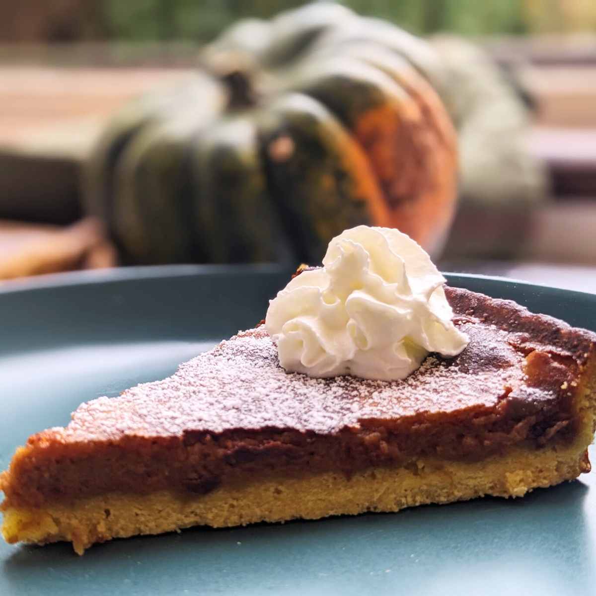 A slice of spicy pumpkin pie on a plate with a dollop of cream on top.