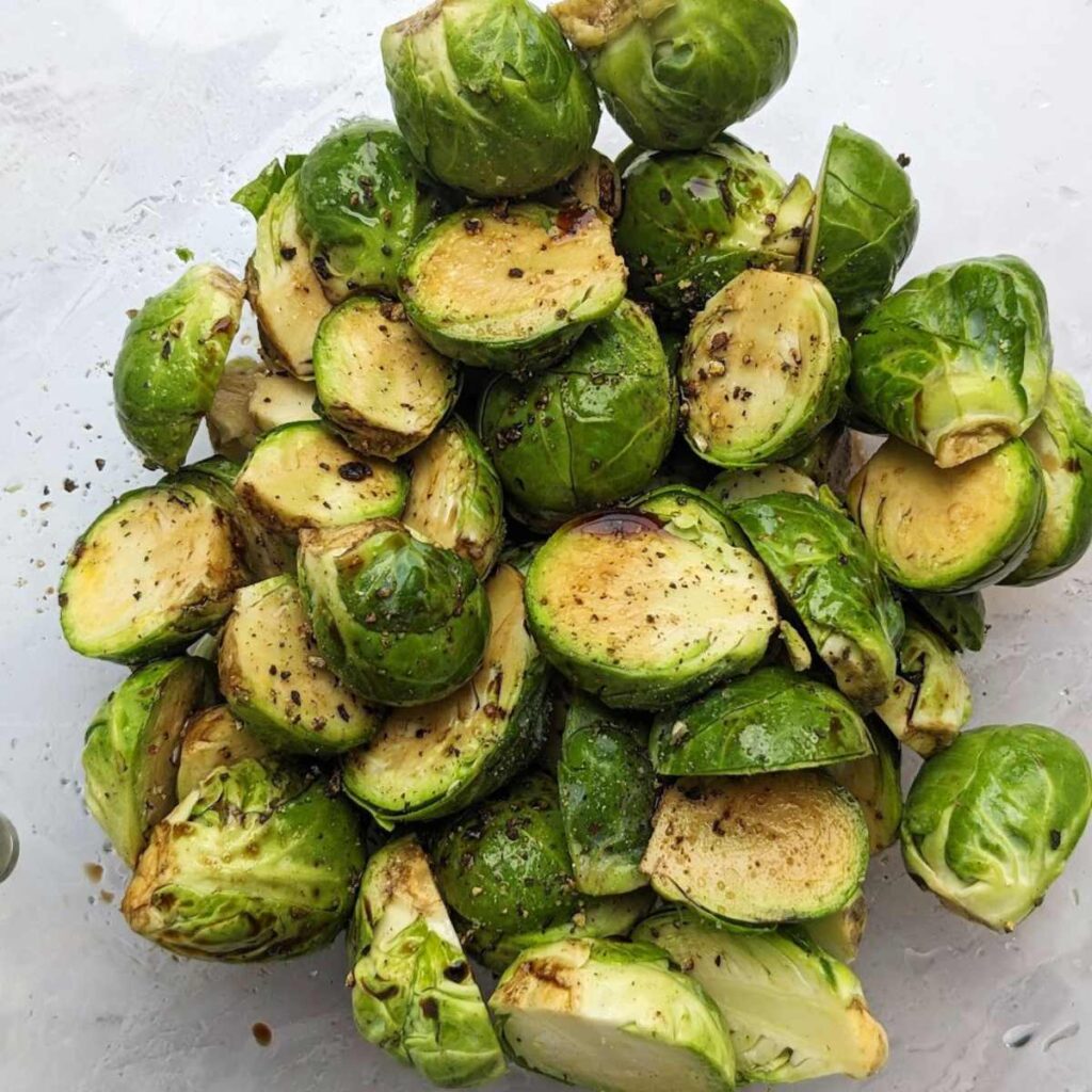 Raw Brussels sprouts cut in half with oil and balsamic vinegar drizzled over them.